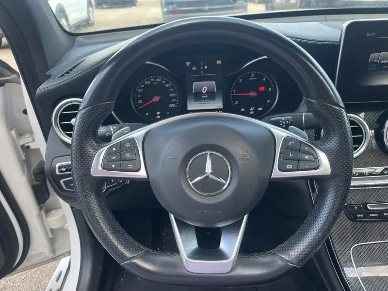 Vue rapprochée du volant cuir perforé noir du Mercedes GLC Coupé blanc diamant avec tableau de bord et compteurs visibles.