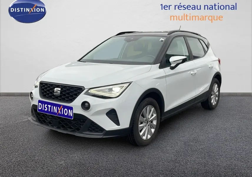 SEAT Arona blanc alpin métal avec toit noir, vue 3/4 avant droit, sur sol gris devant un mur blanc.