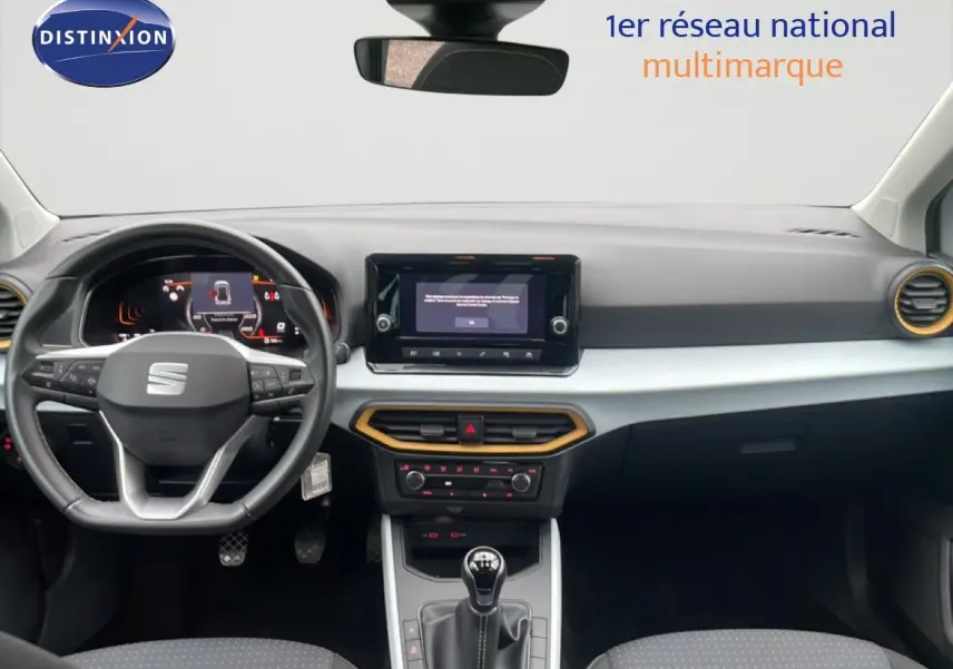 Vue intérieure avant du tableau de bord du SEAT Arona blanc alpin métal, avec volant cuir et touches jaunes autour des aérateurs.