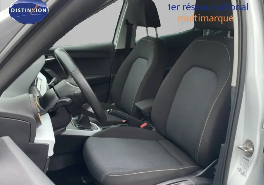 Vue intérieure côté conducteur du SEAT Arona 2025 blanc alpin, montrant les sièges avant en tissu noir et volant multifonction.