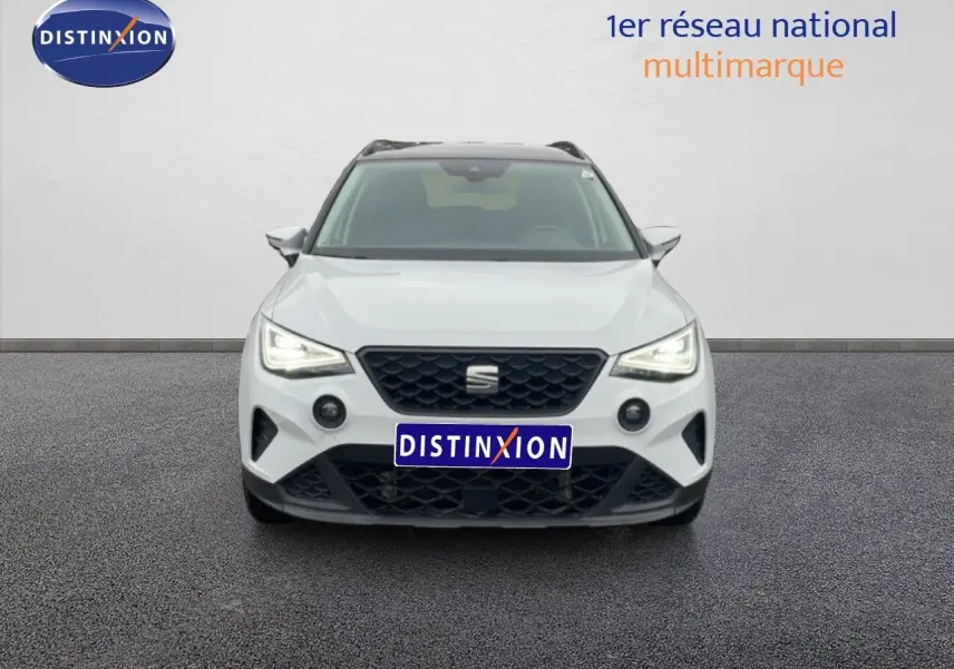 Vue frontale d’un SEAT Arona blanc alpin métal avec toit noir, phares allumés et calandre noire distinctive.