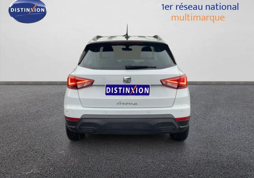 Vue arrière d’un SEAT Arona blanc alpin avec toit noir, feux arrière allumés sur fond neutre.