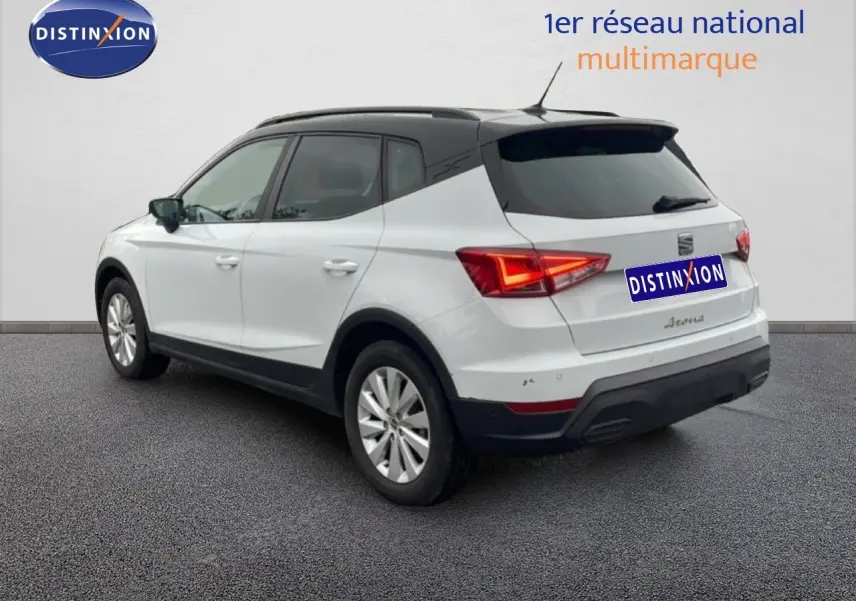 SEAT Arona blanc alpin métal avec toit noir, vue 3/4 arrière côté gauche, feux arrière allumés.