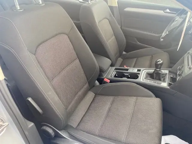 Vue intérieure côté conducteur de la Volkswagen Passat 2015, sièges tissu gris et levier de vitesse manuel visible.