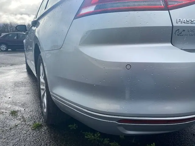 Vue 3/4 arrière droite d'une Volkswagen Passat reflet d'argent 2015 avec capteur de recul visible sur le pare-chocs.
