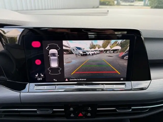Écran central de la Volkswagen Golf VIII hybride montrant la caméra de recul avec guidage coloré en extérieur.