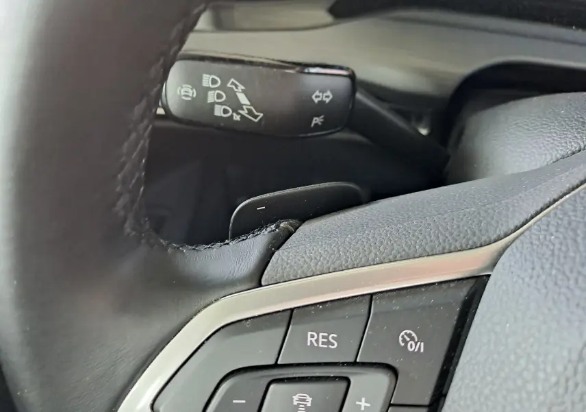 Gros plan sur les commandes au volant en cuir noir de la Volkswagen Golf VIII hybride rechargeable, avec régulateur de vitesse.