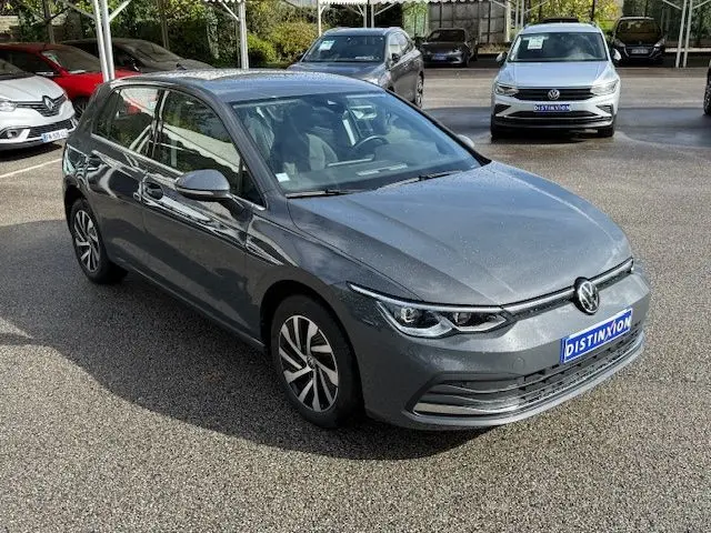 Volkswagen Golf VIII 1.4 e-Hybrid gris dauphin vue 3/4 avant droit sur parking avec logo Distinxion visible.