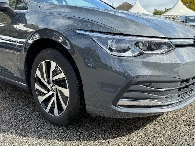 Gros plan sur l'avant gauche d'une Volkswagen Golf VIII gris dauphin, mettant en valeur le phare LED et la jante alliage.