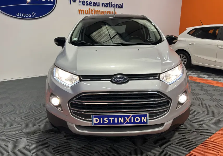 Vue avant d'un Ford EcoSport gris 2018 avec phares allumés et plaque Distinxion en intérieur showroom.