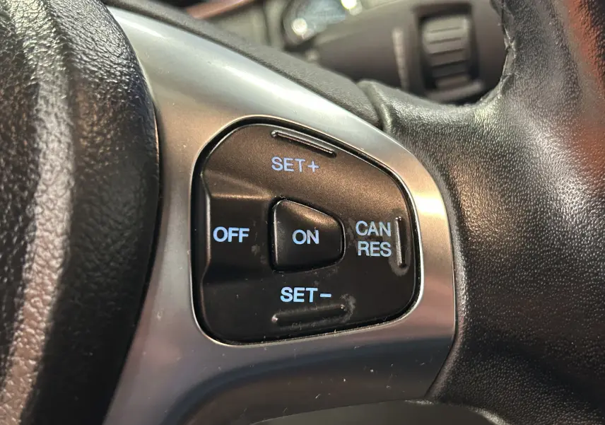 Gros plan sur les commandes de régulateur de vitesse au volant cuir noir d'un Ford EcoSport gris Titanium 2018.