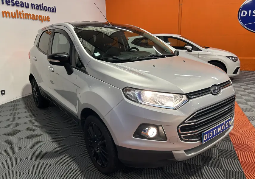 Ford EcoSport gris en 3/4 avant droit avec phares et antibrouillards allumés dans un showroom.