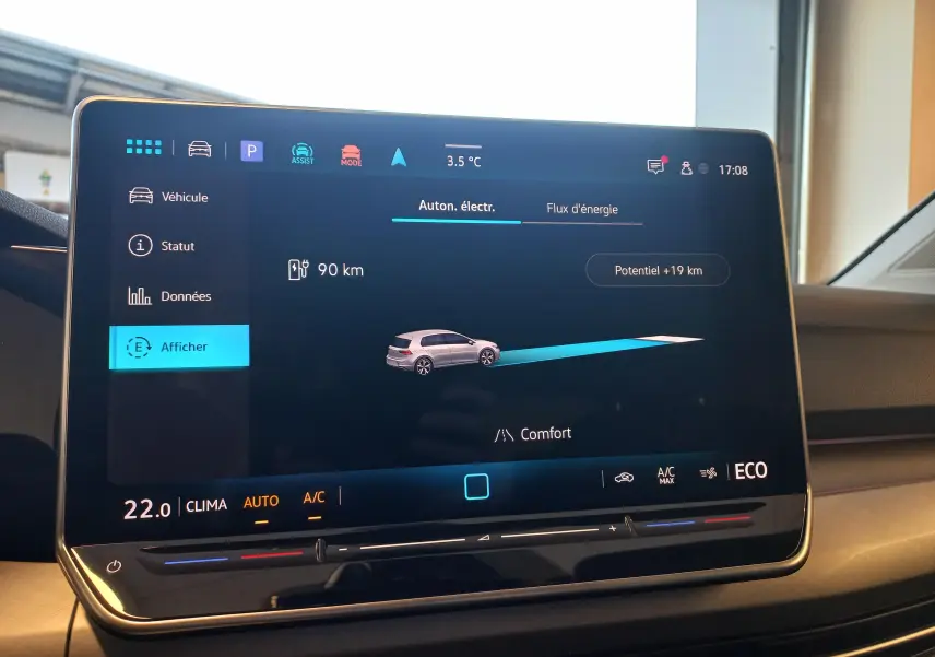 Écran tactile intérieur de la Volkswagen Golf 1.5 eHybrid 2025 montrant l'autonomie électrique et les réglages climatiques.