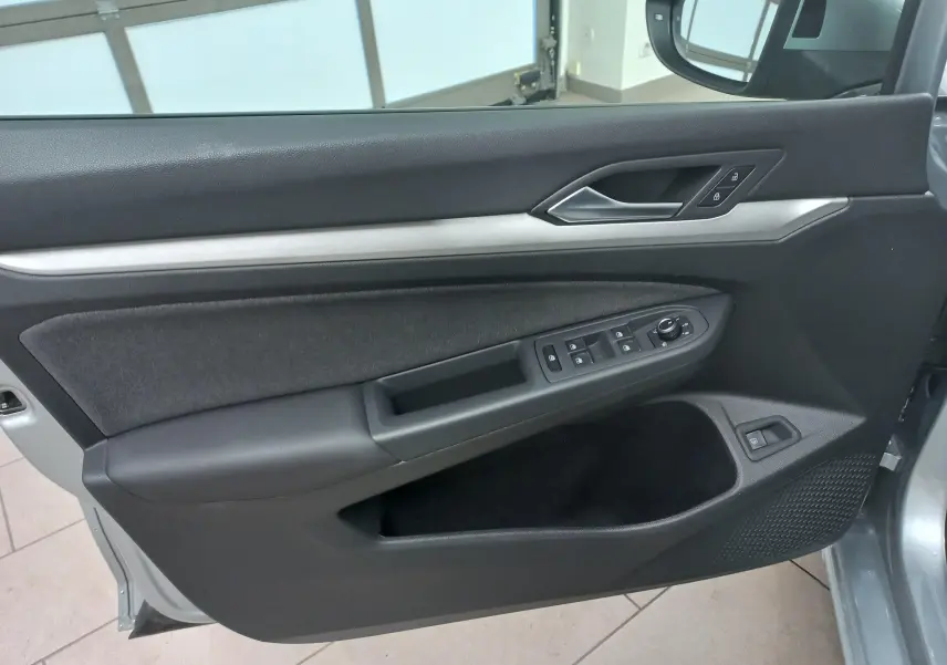 Vue intérieure du panneau de porte avant gauche de la Volkswagen Golf 1.5 eHybrid 2025 en Argent Dolomite avec commandes électriques.