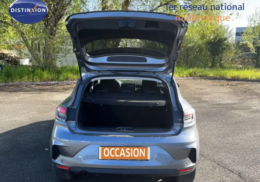 Vue arrière d'une Renault Clio gris schiste métal 2025 avec coffre ouvert, stationnée en extérieur sur sol goudronné.