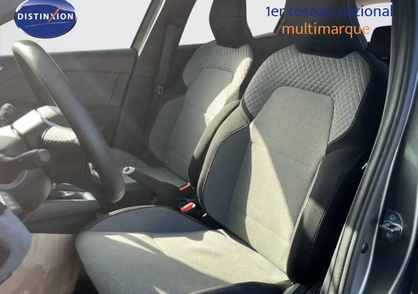 Vue intérieure côté conducteur de la Renault Clio 2025, sièges tissu gris et noir avec surpiqûres apparentes.