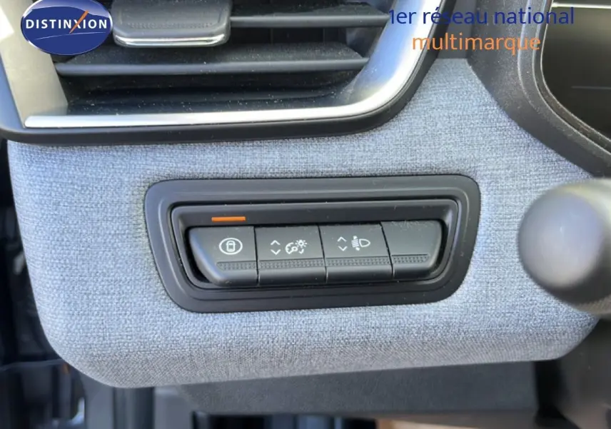 Gros plan sur les commandes d'éclairage intégrées dans la garniture tissu gris clair du tableau de bord de la Renault Clio 2025.