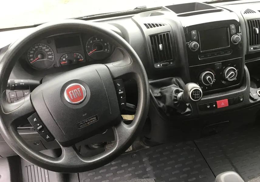 Vue intérieure du tableau de bord du Fiat Ducato Fourgon 2021, volant noir avec logo rouge et levier de vitesse manuel.