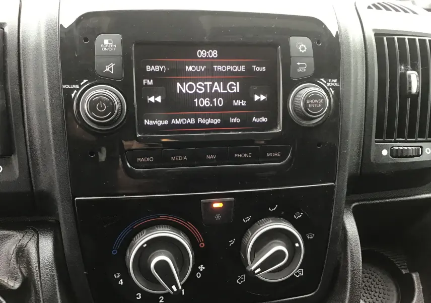 Vue rapprochée du tableau de bord noir du Fiat Ducato Fourgon 2021, avec écran radio affichant la station Nostalgie.