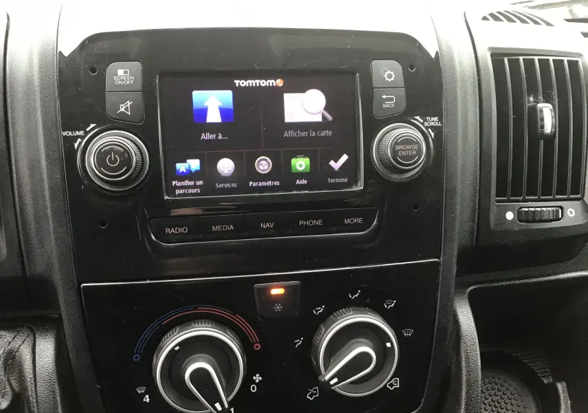 Vue rapprochée du tableau de bord noir du Fiat Ducato Fourgon 2021, avec écran tactile TomTom et commandes de climatisation.