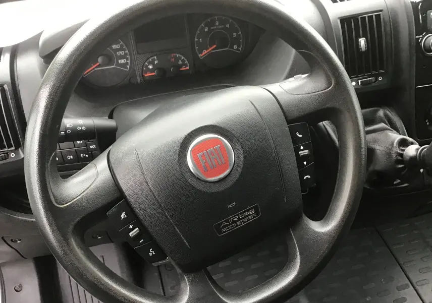 Vue intérieure centrée sur le volant noir du Fiat Ducato Fourgon blanc, avec commandes intégrées visibles sur le volant.