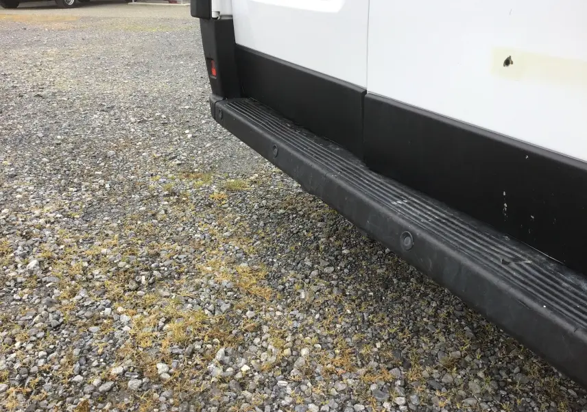 Détail du bas de caisse côté droit du FIAT Ducato Fourgon blanc, avec marchepied noir et capteurs de stationnement.