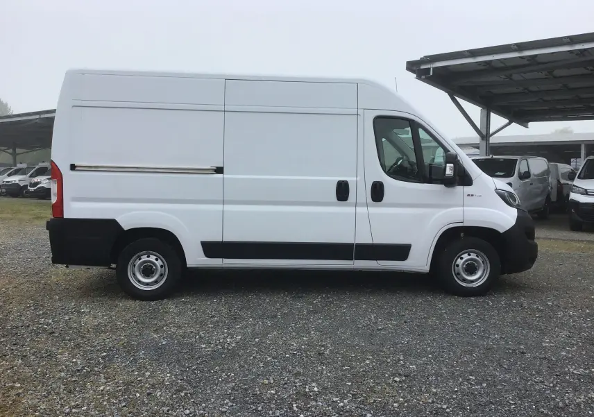 Fiat Ducato Fourgon blanc vu de profil côté droit, avec porte coulissante et protections noires sur bas de caisse.