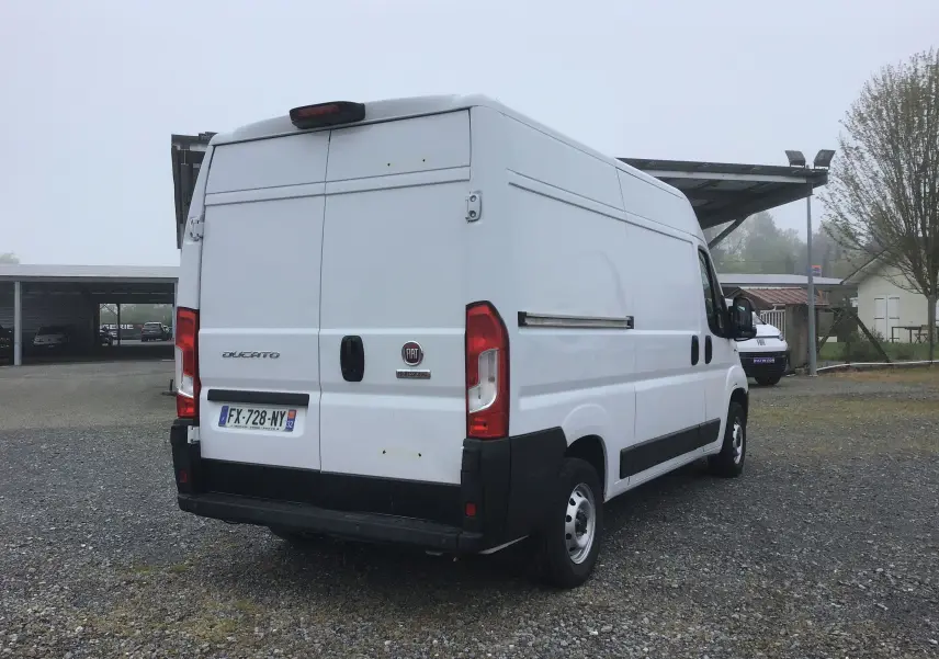 Vue 3/4 arrière droite d'un FIAT Ducato Fourgon blanc, avec portes arrière fermées et pare-chocs noir.