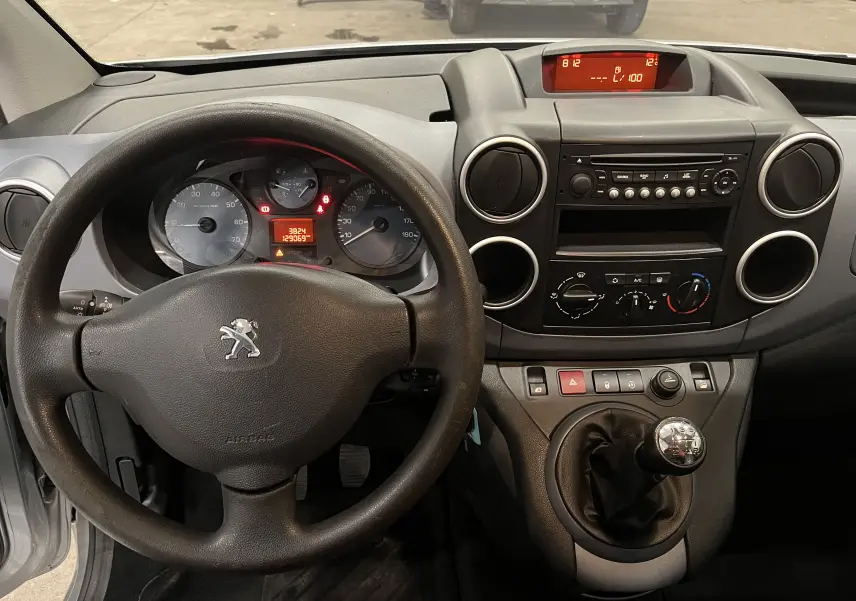 Vue intérieure du tableau de bord et volant noir du Peugeot Partner Tepee gris aluminium, avec levier de vitesses manuel visible.