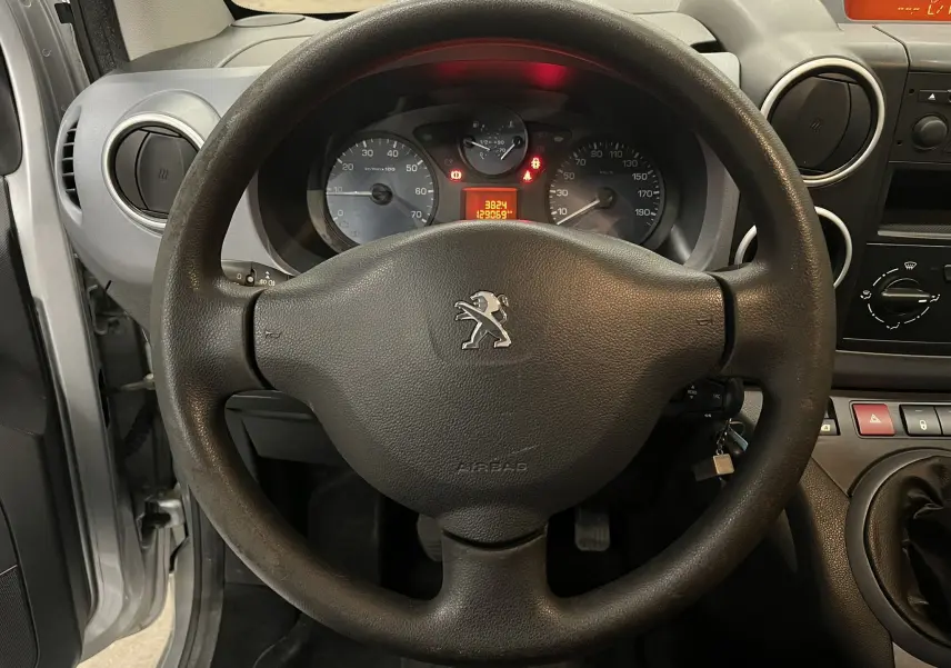 Vue intérieure centrée sur le volant noir avec logo Peugeot et tableau de bord du Partner Tepee gris aluminium.