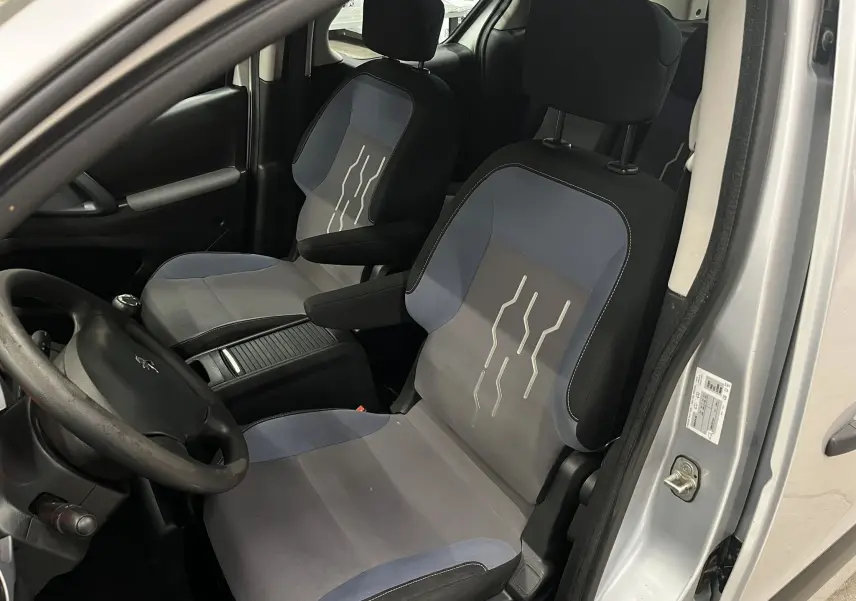 Vue intérieure côté conducteur du Peugeot Partner Tepee gris aluminium, sièges tissu bicolore avec motifs clairs.