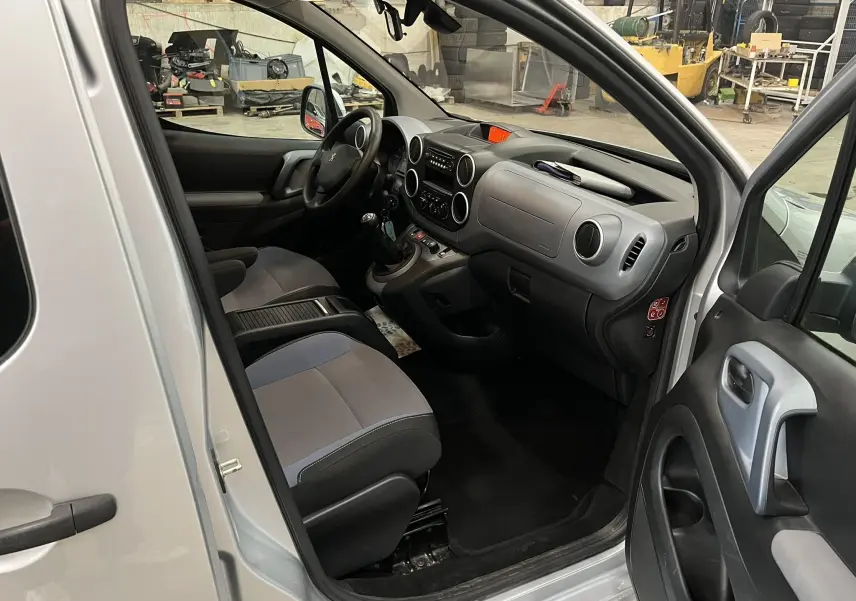 Vue intérieure côté conducteur d'un Peugeot Partner Tepee gris aluminium, montrant le tableau de bord et les sièges en tissu bicolore.