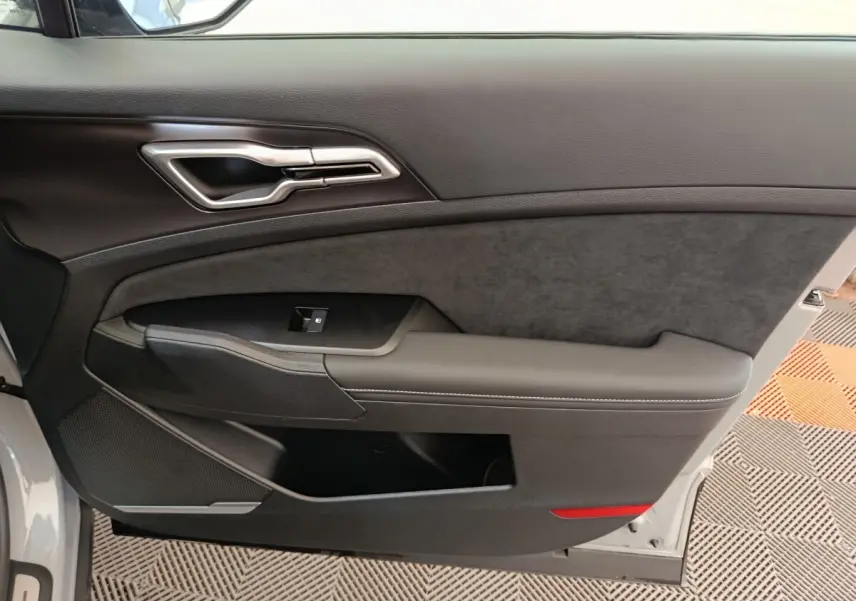 Intérieur côté gauche de la porte avant gris clair du Kia Sportage 2026 avec poignée alu et accoudoir en cuir.