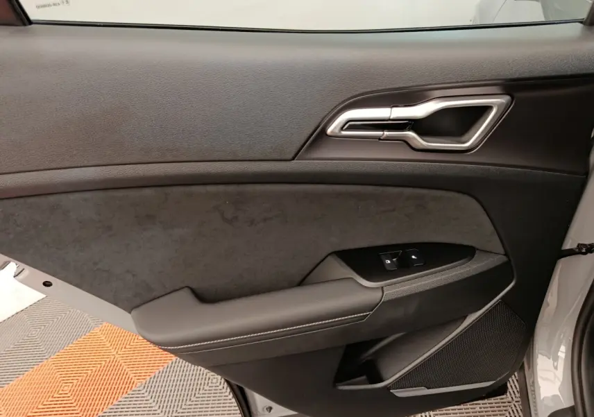 Vue intérieure côté gauche de la porte avant gris clair du KIA SPORTAGE 2026 avec garniture noire et commandes fenêtres.