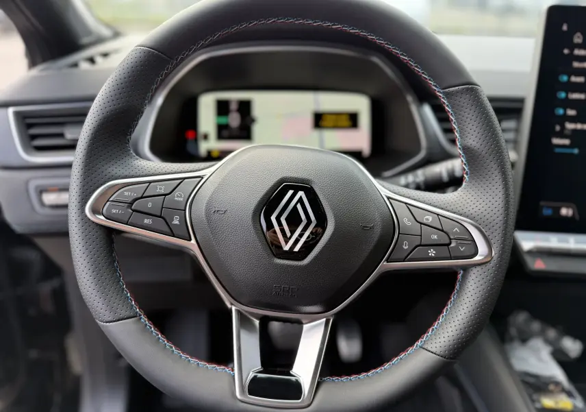 Volant en cuir noir avec surpiqûres tricolores du Renault Captur 2025, vue rapprochée du tableau de bord numérique.