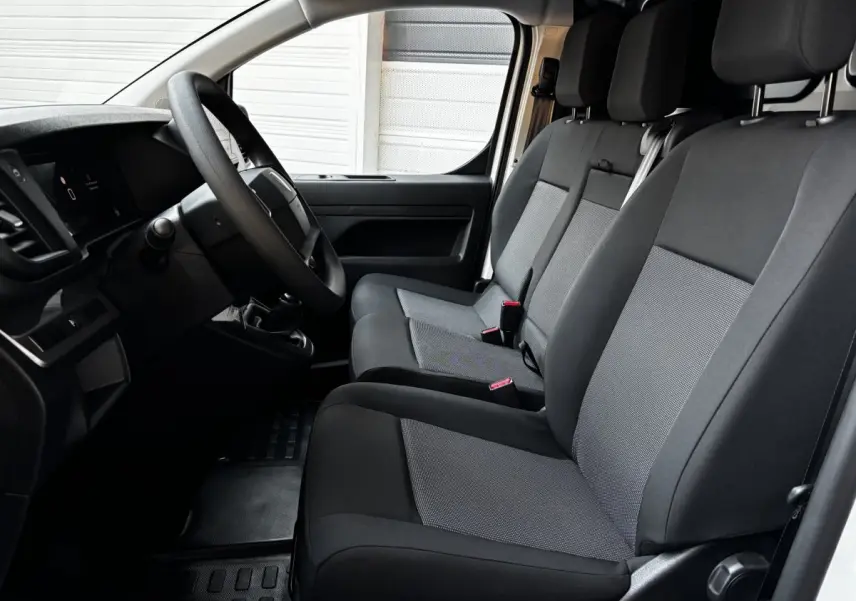 Vue intérieure côté conducteur du Peugeot Expert Fourgon blanc 2025, montrant les sièges avant en tissu gris et noir.
