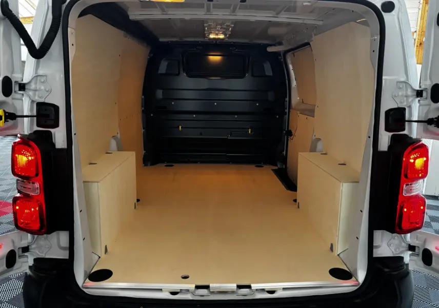 Intérieur du coffre blanc Peugeot Expert Fourgon Taille M 2025, vue arrière ouverte avec plancher et parois en bois clair.