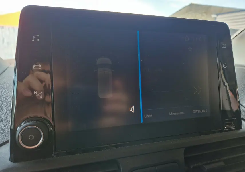 Écran tactile central du tableau de bord du Peugeot Partner gris Artense, affichant l'aide au stationnement.