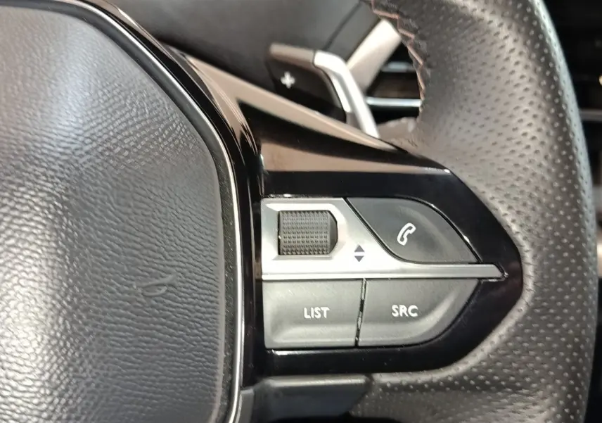 Gros plan sur les commandes gauche du volant en cuir perforé du Peugeot 5008 bleu, boutons multifonctions visibles.