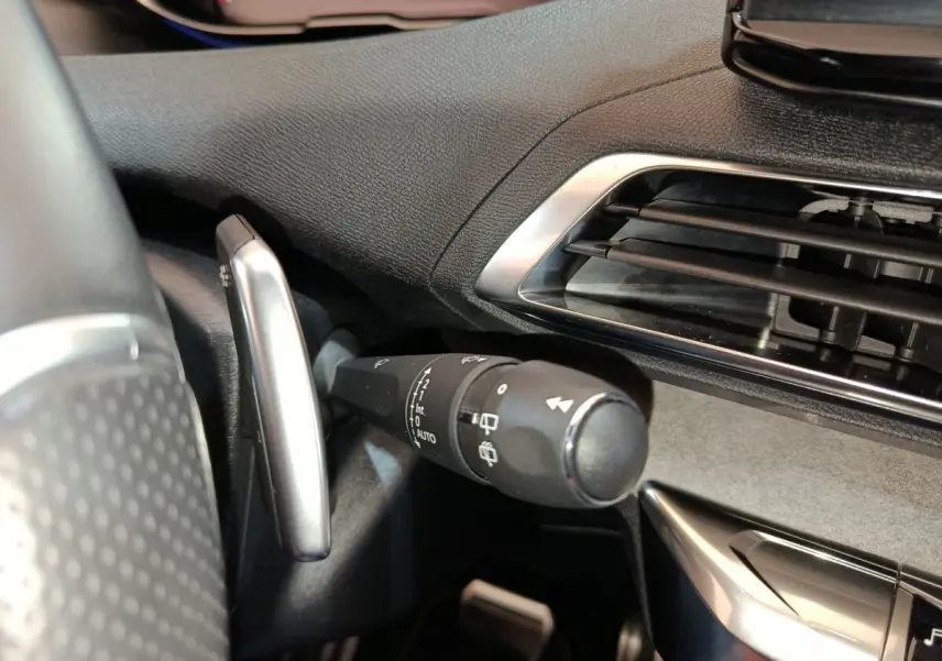 Gros plan sur la commande d’essuie-glace à gauche du volant dans l’habitacle noir du Peugeot 5008 bleu.