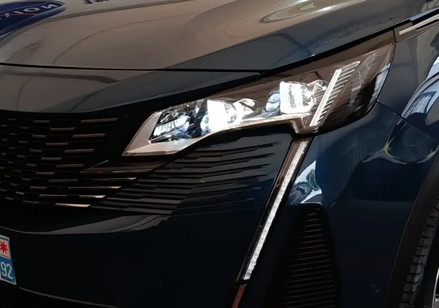 Gros plan sur l'avant droit bleu du Peugeot 5008 2023, mettant en valeur le phare LED et la calandre noire.