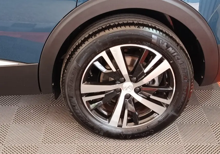 Gros plan sur la roue arrière droite d’un Peugeot 5008 bleu 2023, jante alliage bicolore et pneu Michelin.