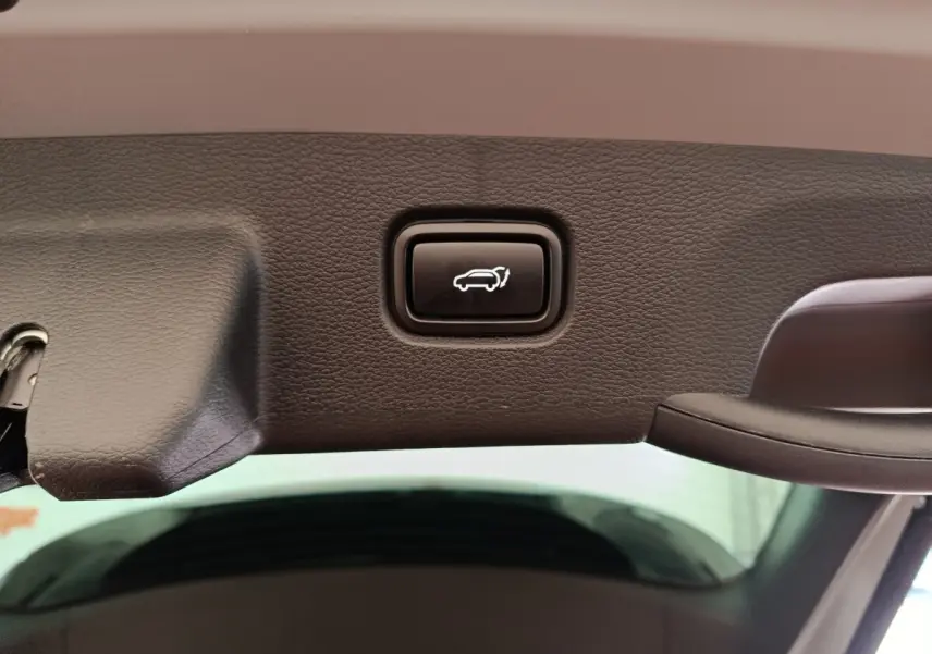 Bouton d'ouverture électrique du coffre sur le bord intérieur du hayon du Kia Sportage gris foncé.