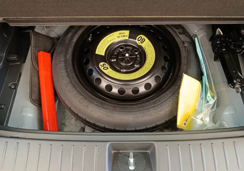Vue plongeante sur la roue de secours noire et ses accessoires dans le coffre d’un Kia Sportage gris foncé.