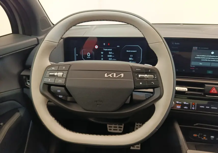 Vue rapprochée du volant bicolore gris clair et noir du Kia Sportage 2026 avec tableau de bord numérique en arrière-plan.
