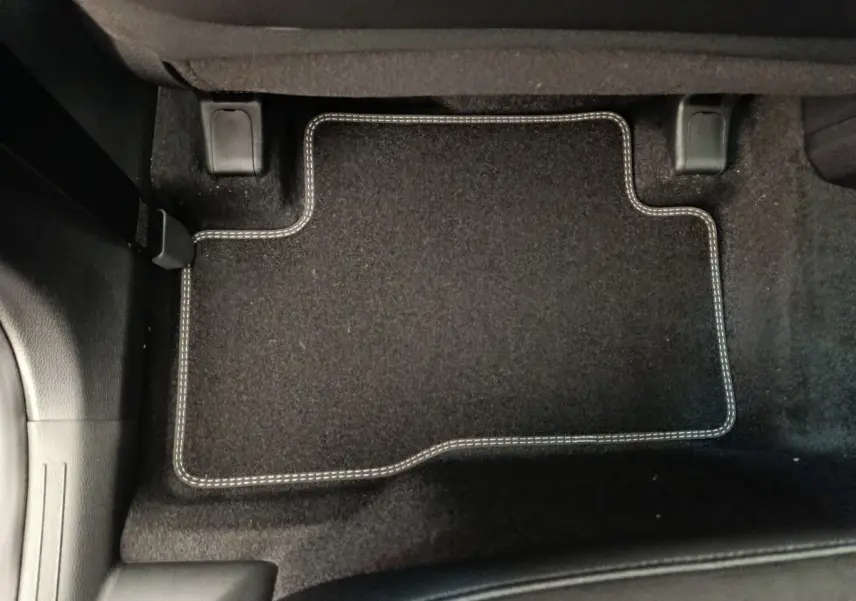 Tapis de sol noir avec surpiqûres blanches côté conducteur d'un KIA Sportage gris foncé, vue intérieure au sol.