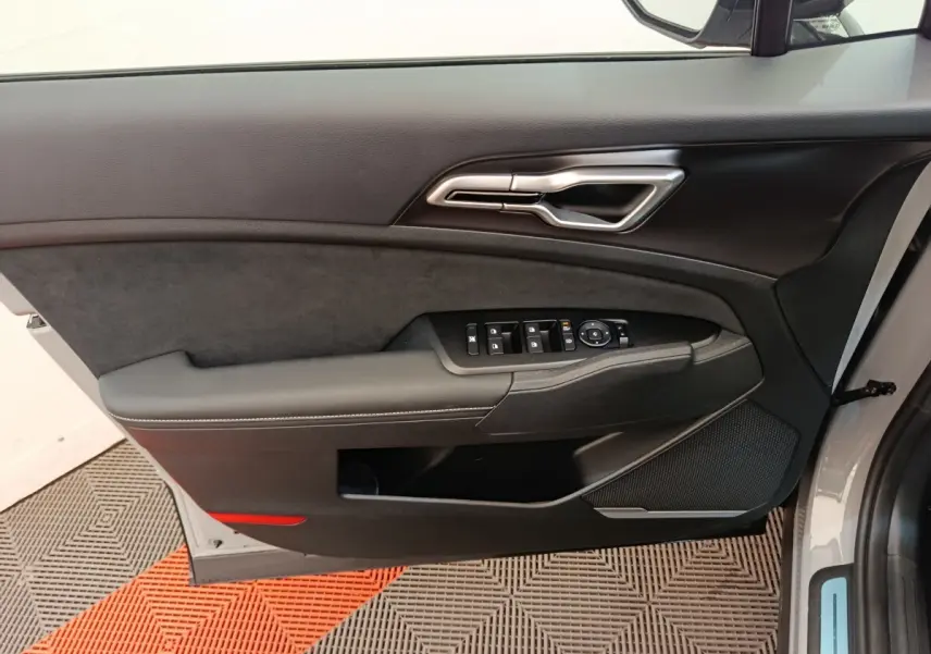 Vue intérieure côté gauche de la porte avant gris foncé du Kia Sportage 2026 avec commandes de vitres et poignée argentée.