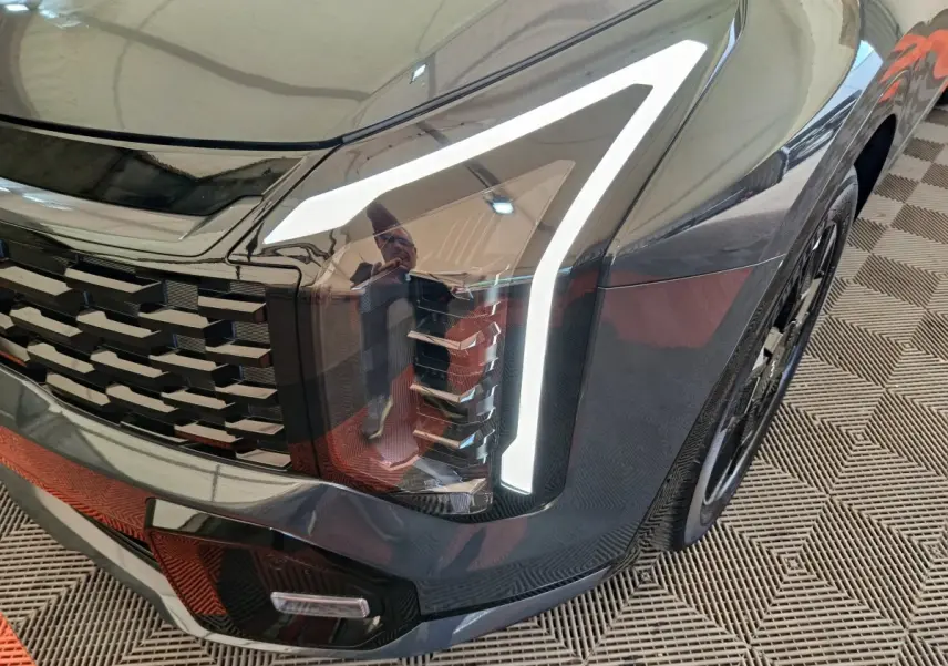 Gros plan sur l'avant droit gris foncé du KIA SPORTAGE 2026, mettant en valeur le phare LED et la calandre distinctive.