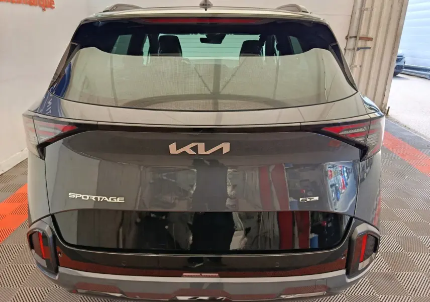 Vue arrière d'un KIA Sportage gris foncé avec logo moderne et feux arrière intégrés au hayon noir brillant.