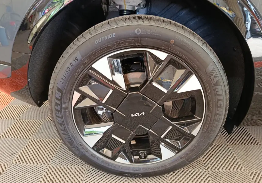 Gros plan sur la roue avant droite du KIA SPORTAGE gris foncé, mettant en valeur la jante noire et chromée au design géométrique.